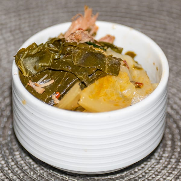 A white bowl filled with Ridiculous Eatz's southern collard greens and cabbage, topped with meat.