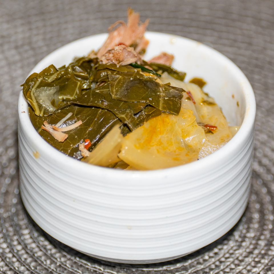 A white bowl filled with Ridiculous Eatz's southern collard greens and cabbage, topped with meat.