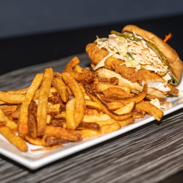 Crispy fried chicken sandwich with coleslaw and pickles, served with a side of golden french fries.