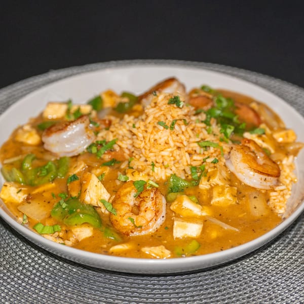 Southern-style shrimp and chicken gumbo with rice, green peppers, and parsley in a white bowl.