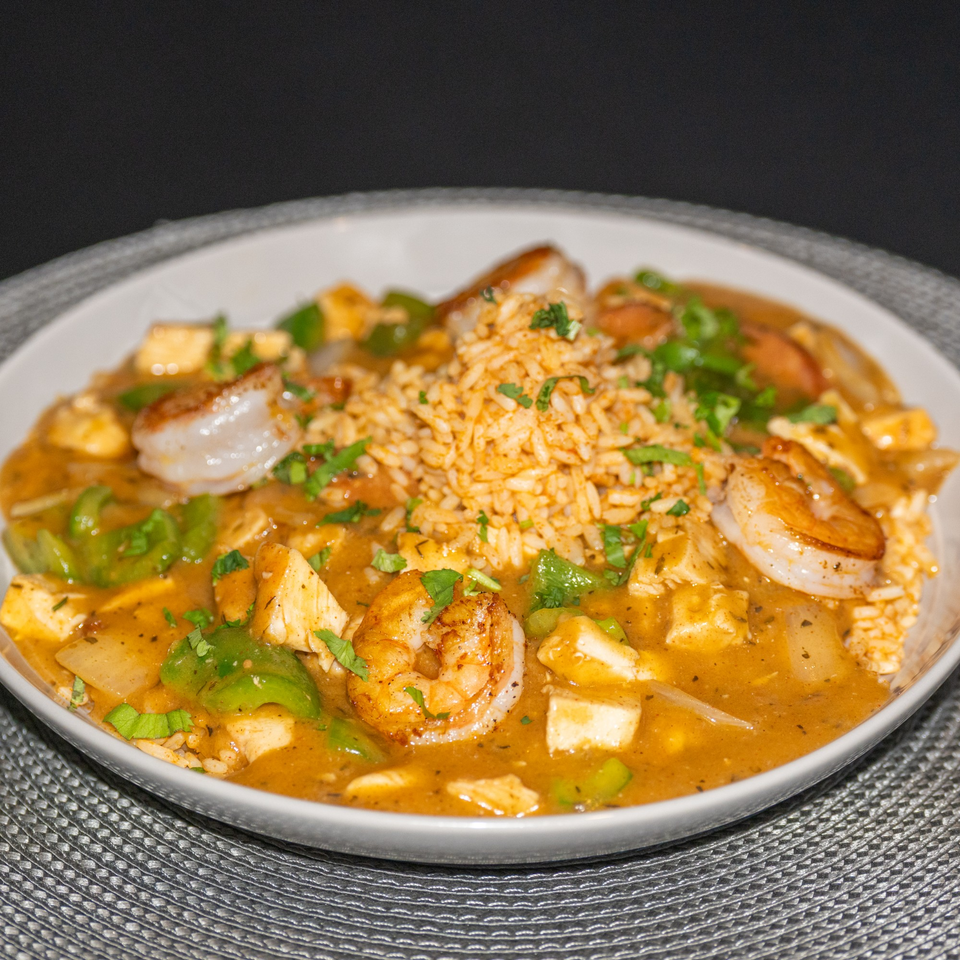 Southern-style shrimp and chicken gumbo with rice, green peppers, and parsley in a white bowl.