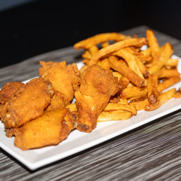 Crispy fried chicken wings and golden french fries on a white rectangular plate.
