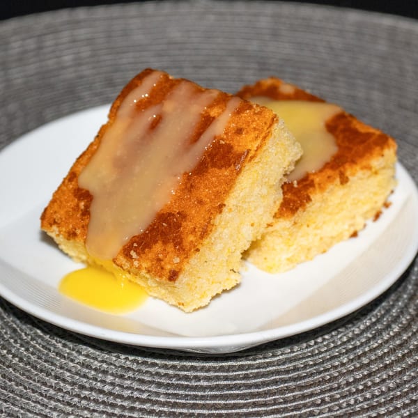 Two pieces of Ridiculous Eatz cornbread, drizzled with a light glaze and a pool of yellow sauce.