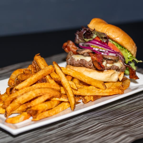 A Ridiculous Eatz burger with bacon, cheese, and vegetables, served with a side of golden fries.